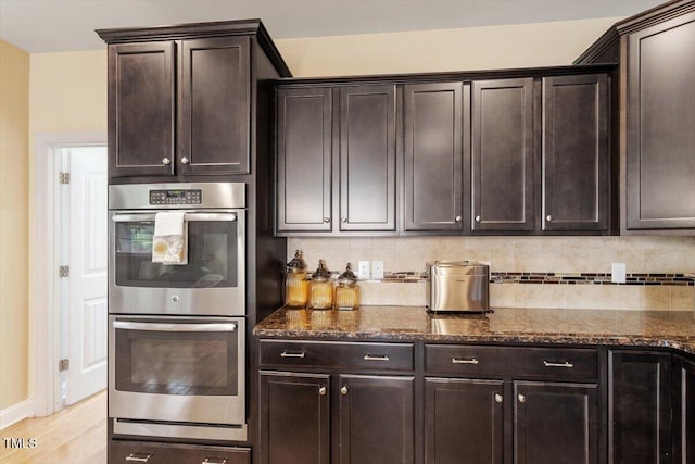 150 Saint Mellion St, Raleigh, NC 27603 - kitchen featuring stainless steel double oven, dark stone countertops, tasteful backsplash, light wood finished floors, and dark brown cabinets