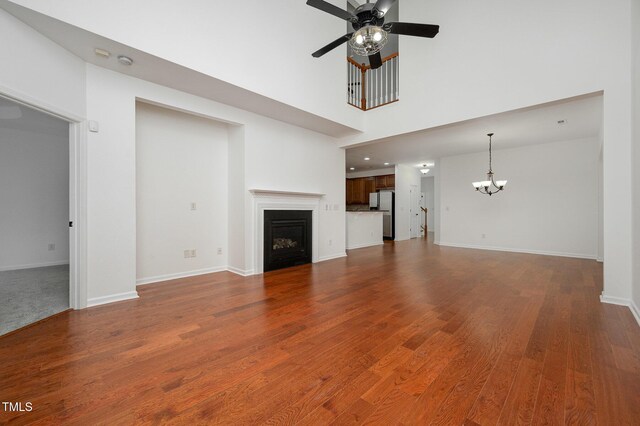 1016 Kingston Grove Dr, Cary, NC 27519 - unfurnished living room featuring a ceiling fan, a chandelier, a fireplace, dark wood-style floors, and a towering ceiling
