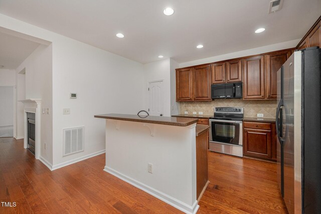 1016 Kingston Grove Dr, Cary, NC 27519 - kitchen with stainless steel appliances, wood finished floors, backsplash, a breakfast bar, and a kitchen island with sink