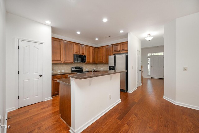 1016 Kingston Grove Dr, Cary, NC 27519 - kitchen with black appliances, wood finished floors, a kitchen breakfast bar, backsplash, and brown cabinetry