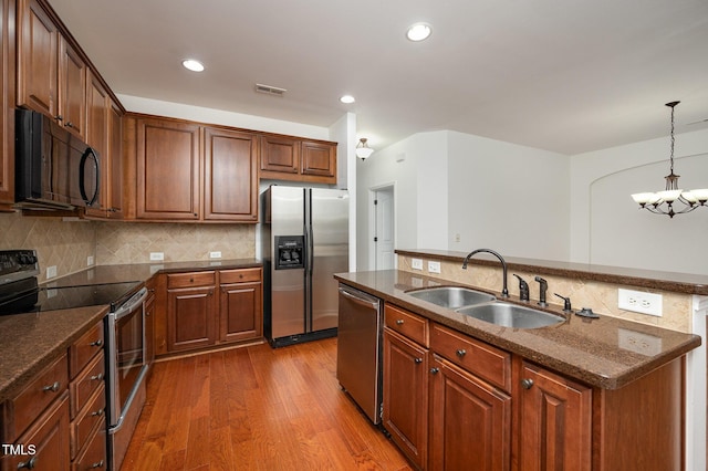 1016 Kingston Grove Dr, Cary, NC 27519 - kitchen featuring appliances with stainless steel finishes, a kitchen island with sink, wood finished floors, backsplash, and a chandelier