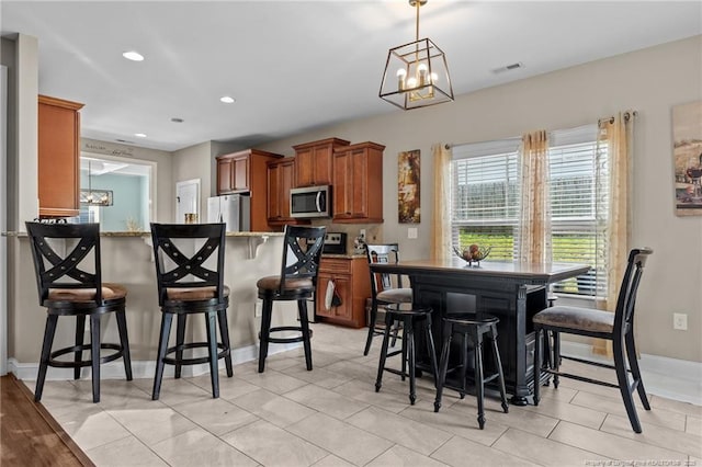 5135 Paul Peel Pl, Hope Mills, NC 28348 - kitchen with stainless steel microwave, freestanding refrigerator, a chandelier, brown cabinetry, and a kitchen bar