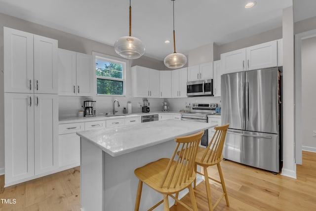 3909 Bristlewood Dr, Durham, NC 27703 - kitchen with stainless steel appliances, light wood-style flooring, a breakfast bar, white cabinetry, and a center island