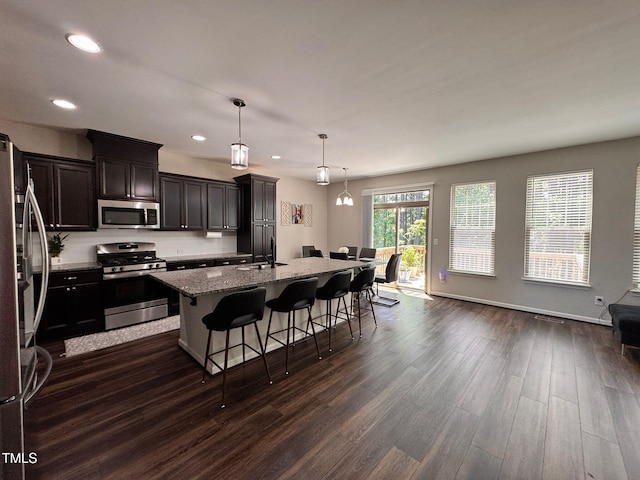 1005 Lathrop Ln, Apex, NC 27523 - kitchen featuring stainless steel appliances, dark wood-style flooring, light stone counters, a breakfast bar area, and a kitchen island with sink