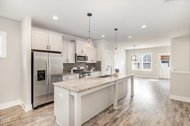 442 Granite Mill Blvd, Chapel Hill, NC 27516 - kitchen with appliances with stainless steel finishes, a kitchen island with sink, light wood-type flooring, light stone counters, and decorative backsplash