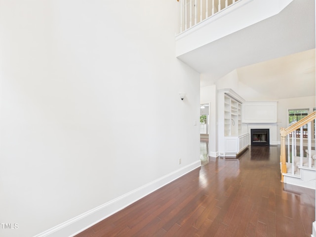 7501 Montibillo Pkwy, Durham, NC 27713 - unfurnished living room featuring dark wood-style flooring, a fireplace, stairs, a high ceiling, and built in features