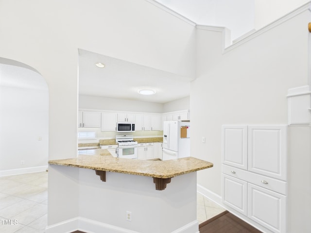 7501 Montibillo Pkwy, Durham, NC 27713 - kitchen featuring white appliances, arched walkways, a kitchen bar, light stone counters, and white cabinetry