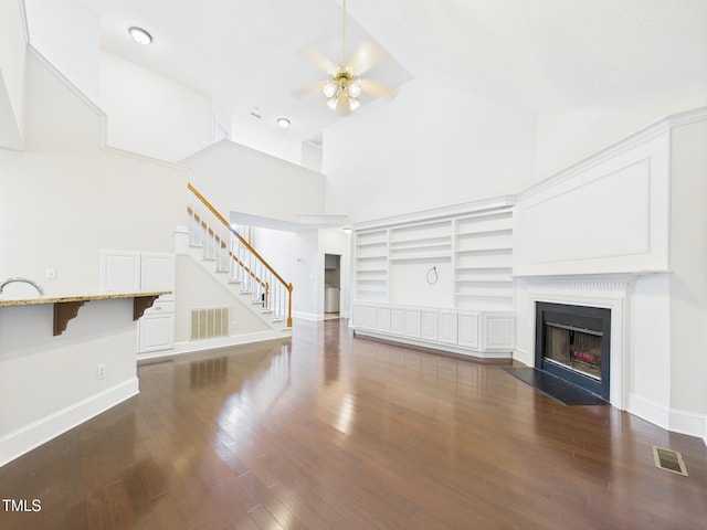 7501 Montibillo Pkwy, Durham, NC 27713 - unfurnished living room with high vaulted ceiling, ceiling fan, a fireplace with flush hearth, stairs, and wood finished floors