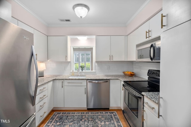 1563 Laureldale Dr, Raleigh, NC 27609 - kitchen featuring stainless steel appliances, white cabinetry, ornamental molding, tasteful backsplash, and light wood-style floors