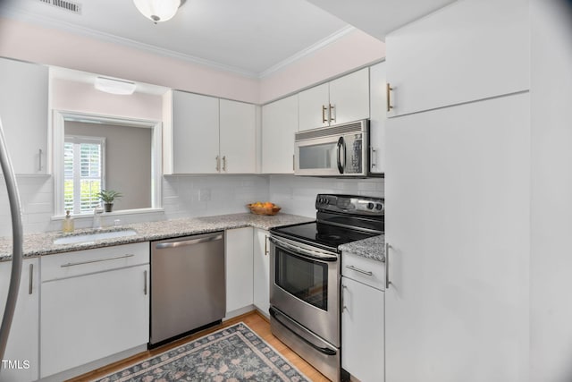 1563 Laureldale Dr, Raleigh, NC 27609 - kitchen featuring appliances with stainless steel finishes, white cabinets, decorative backsplash, ornamental molding, and light wood-style flooring