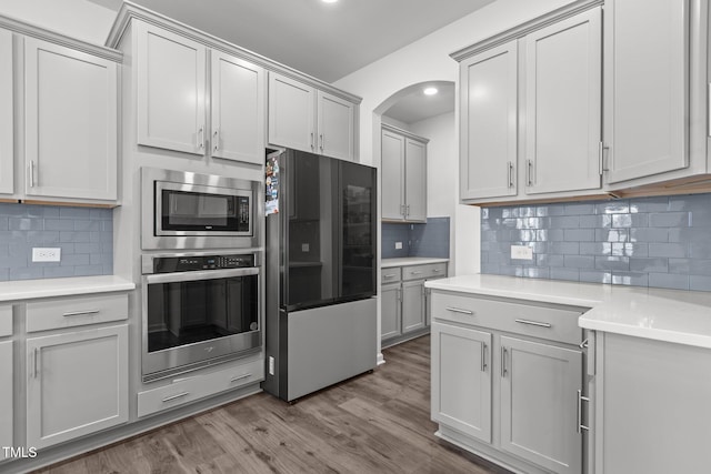 1414 Arena Ln, Fuquay Varina, NC 27526 - kitchen with appliances with stainless steel finishes, arched walkways, backsplash, light countertops, and dark wood finished floors