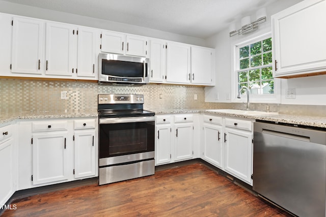 613 Penncross Dr, Raleigh, NC 27610 - kitchen featuring appliances with stainless steel finishes, white cabinetry, dark wood-type flooring, light stone countertops, and tasteful backsplash