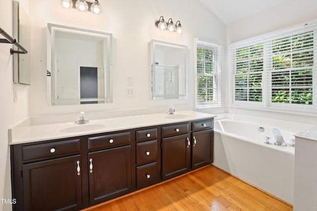 613 Penncross Dr, Raleigh, NC 27610 - bathroom featuring double vanity, a bath, wood finished floors, vaulted ceiling, and a shower