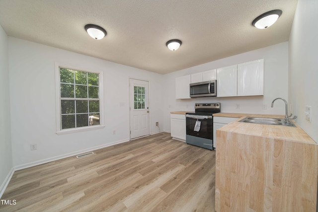 4258 Kaplan Dr, Raleigh, NC 27606 - kitchen featuring appliances with stainless steel finishes, light wood-type flooring, white cabinets, wood counters, and a textured ceiling