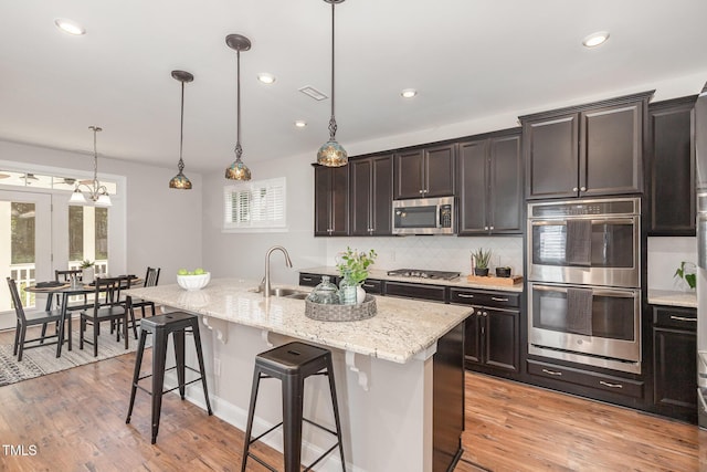 1127 Timbercut Dr, Durham, NC 27703 - kitchen featuring appliances with stainless steel finishes, backsplash, a kitchen island with sink, light wood-style flooring, and recessed lighting