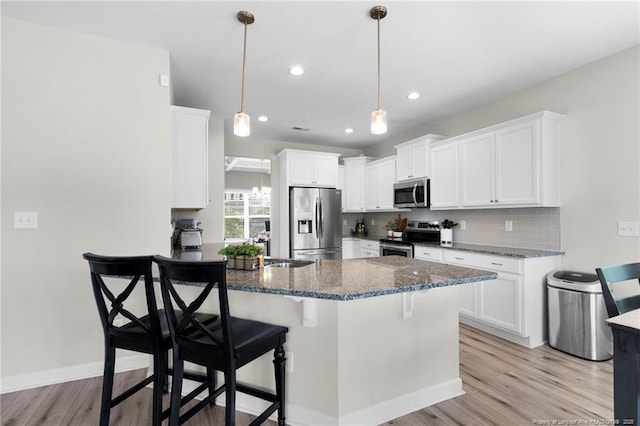 3902 Standardbred Dr, Hope Mills, NC 28348 - kitchen with appliances with stainless steel finishes, a peninsula, light wood-style floors, dark stone counters, and a kitchen breakfast bar