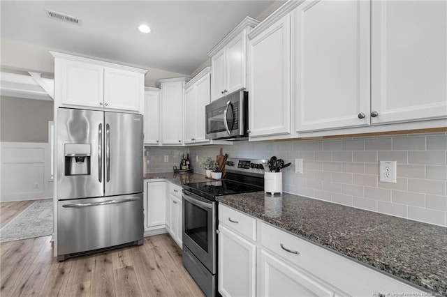 3902 Standardbred Dr, Hope Mills, NC 28348 - kitchen featuring appliances with stainless steel finishes, light wood finished floors, white cabinetry, dark stone counters, and tasteful backsplash