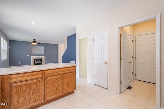 2241 Spruce Shadows Ln, Raleigh, NC 27614 - kitchen featuring light floors, ceiling fan, a glass covered fireplace, and brown cabinetry