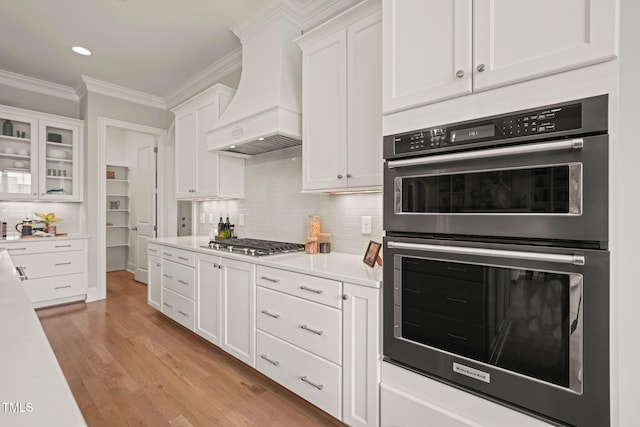 121 Hardy Oaks Way, Holly Springs, NC 27540 - kitchen with double oven, custom exhaust hood, stainless steel gas stovetop, white cabinetry, and ornamental molding