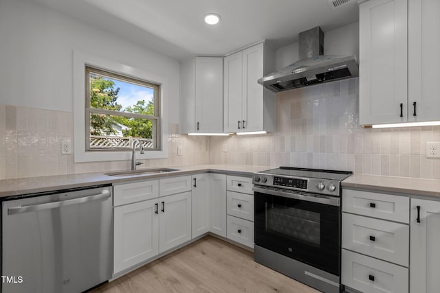 620 Red Carriage Ave, Durham, NC 27704 - kitchen featuring stainless steel appliances, wall chimney exhaust hood, light countertops, light wood finished floors, and white cabinetry