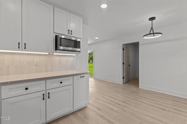 620 Red Carriage Ave, Durham, NC 27704 - kitchen with stainless steel microwave, light wood-type flooring, decorative backsplash, white cabinets, and light countertops