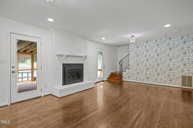 3516 Swift Dr, Raleigh, NC 27606 - unfurnished living room with wood finished floors, a brick fireplace, stairway, recessed lighting, and wallpapered walls