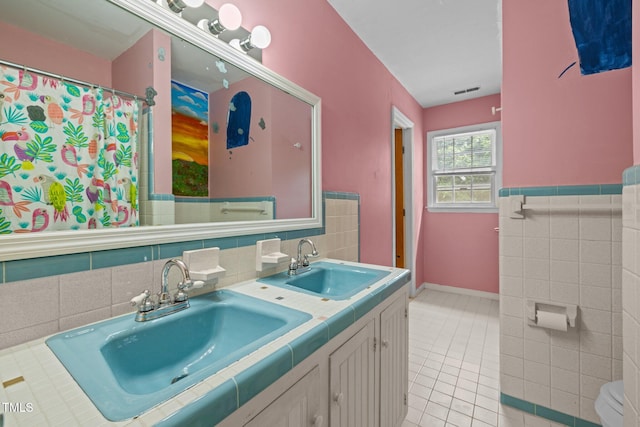 3516 Swift Dr, Raleigh, NC 27606 - full bathroom featuring tile walls, double vanity, tile patterned floors, and a wainscoted wall