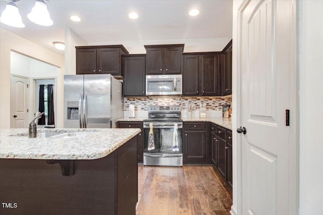 51 Balboa Pkwy, Clayton, NC 27520 - kitchen with stainless steel appliances, dark brown cabinetry, wood finished floors, light stone counters, and backsplash