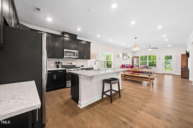 1247 White Flint Cir, Durham, NC 27703 - kitchen with appliances with stainless steel finishes, dark cabinetry, crown molding, a breakfast bar area, and wood finished floors