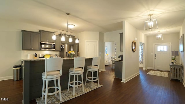 966 Airedale Trl, Garner, NC 27529 - kitchen featuring appliances with stainless steel finishes, dark wood finished floors, a kitchen breakfast bar, gray cabinets, and tasteful backsplash