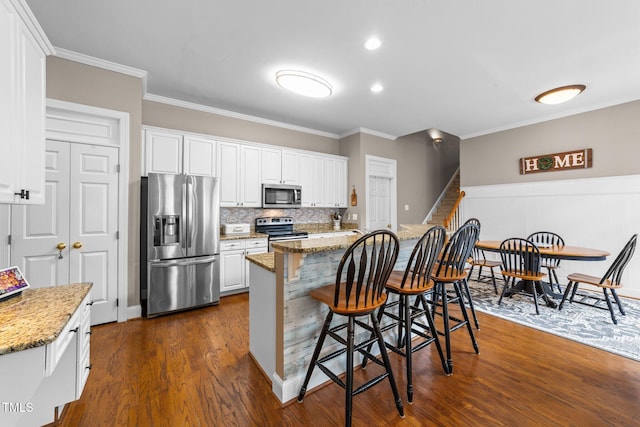 124 Kingsport Rd, Holly Springs, NC 27540 - kitchen featuring stainless steel appliances, a breakfast bar, dark wood-style floors, ornamental molding, and white cabinets