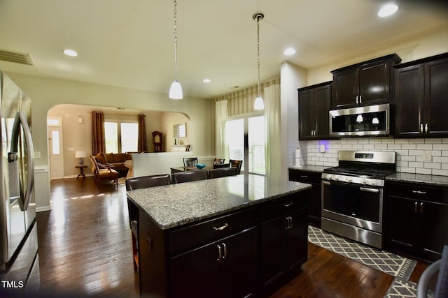 83 Mariners Point Way, Garner, NC 27529 - kitchen featuring appliances with stainless steel finishes, arched walkways, tasteful backsplash, a center island, and stone countertops