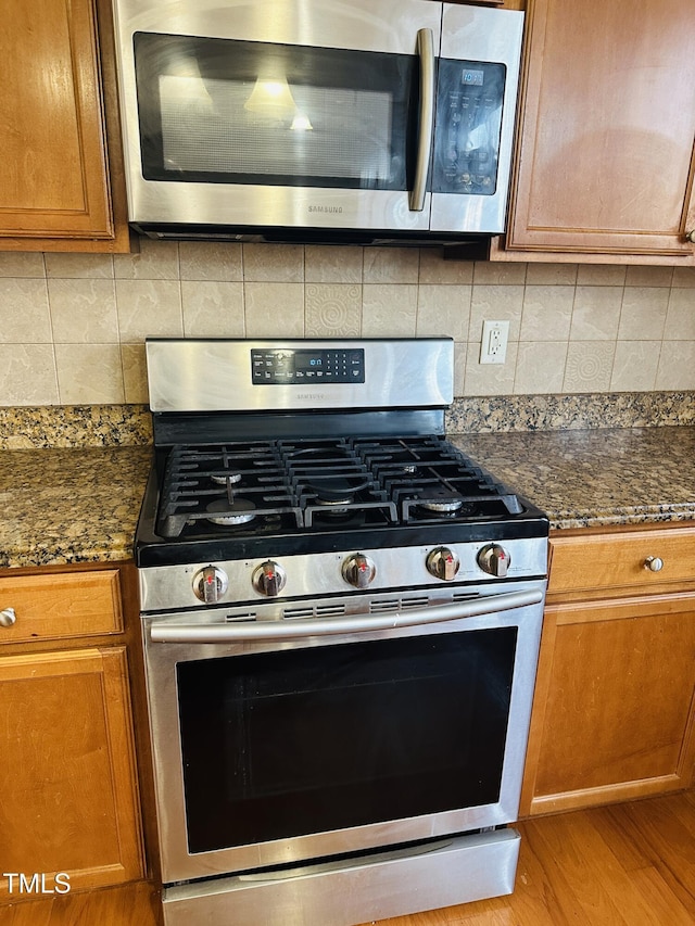 1150 Brookhill Way, Cary, NC 27519 - kitchen featuring stainless steel appliances, light wood-style flooring, brown cabinetry, dark stone countertops, and backsplash
