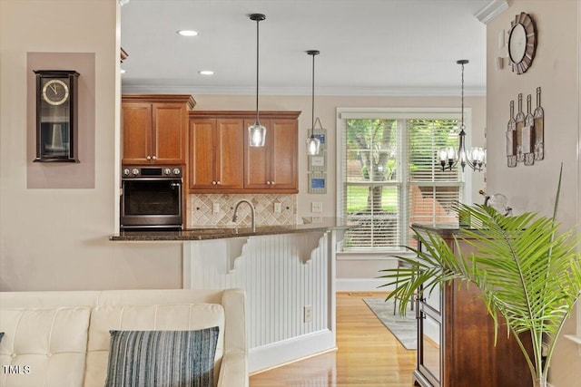 10012 San Remo Pl, Wake Forest, NC 27587 - kitchen featuring oven, brown cabinetry, a kitchen bar, tasteful backsplash, and light wood-type flooring