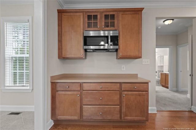 259 Rolling Pines Dr, Spring Lake, NC 28390 - kitchen featuring stainless steel microwave, brown cabinets, light countertops, glass insert cabinets, and ornamental molding