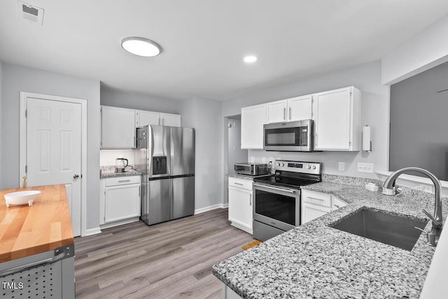611 Quartz Dr, Durham, NC 27703 - kitchen featuring appliances with stainless steel finishes, light stone counters, white cabinets, light wood-style floors, and recessed lighting