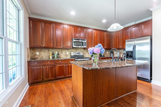 9701 Corktree Ct, Wake Forest, NC 27587 - kitchen with stainless steel appliances, light wood-style flooring, dark stone countertops, hanging light fixtures, and ornamental molding
