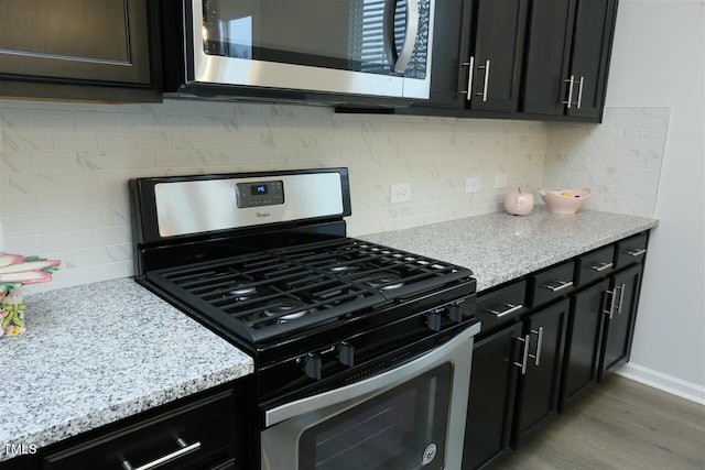 319 Great Northern Sta, Apex, NC 27502 - kitchen featuring appliances with stainless steel finishes, tasteful backsplash, light wood-type flooring, dark cabinetry, and light stone counters
