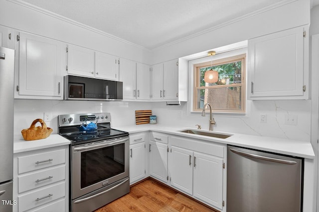 810 Royal Oaks Dr, Durham, NC 27712 - kitchen with stainless steel appliances, light countertops, white cabinets, crown molding, and light wood-style flooring