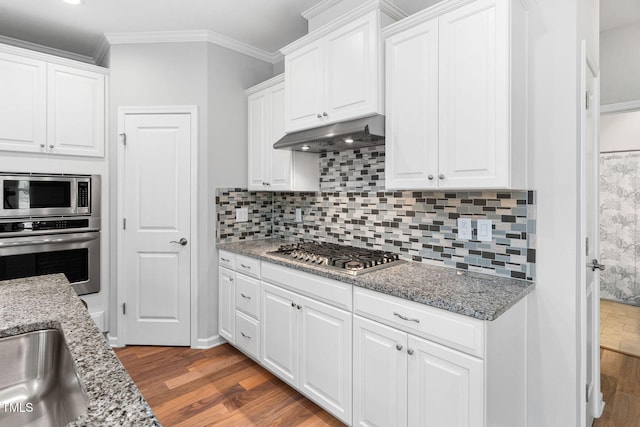1019 Santiago St, Durham, NC 27703 - kitchen with appliances with stainless steel finishes, wood finished floors, under cabinet range hood, white cabinetry, and crown molding