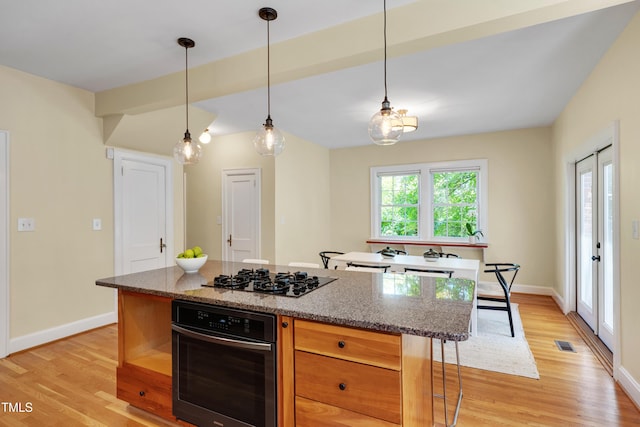 1007 W Markham Ave, Durham, NC 27701 - kitchen with black appliances, light wood finished floors, a center island, decorative light fixtures, and stone counters