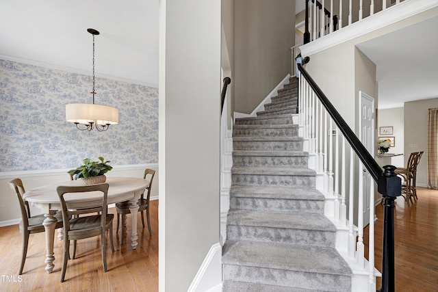 8841 Deerland Grove Dr, Raleigh, NC 27615 - staircase featuring wood finished floors, a wainscoted wall, wallpapered walls, and a chandelier