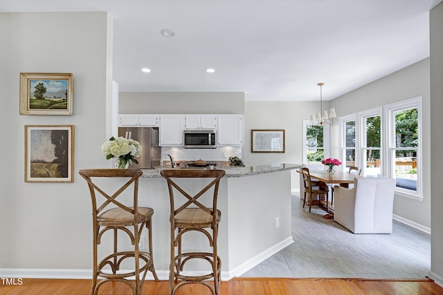 8841 Deerland Grove Dr, Raleigh, NC 27615 - kitchen with appliances with stainless steel finishes, light stone counters, white cabinets, a breakfast bar area, and decorative light fixtures