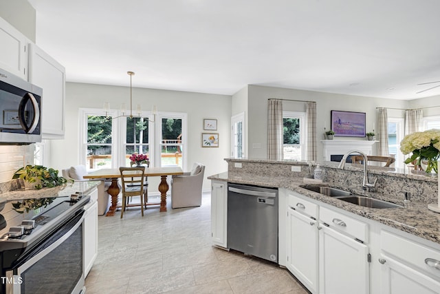 8841 Deerland Grove Dr, Raleigh, NC 27615 - kitchen featuring appliances with stainless steel finishes, light stone counters, white cabinetry, a fireplace, and decorative light fixtures