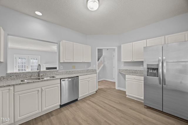 4406 Still Pines Dr, Raleigh, NC 27613 - kitchen featuring stainless steel appliances, white cabinetry, a textured ceiling, light wood-type flooring, and light stone countertops