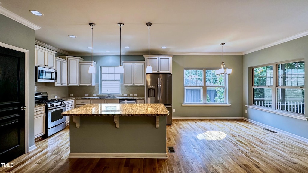621 Ancient Oaks Dr, Holly Springs, NC 27540 - kitchen featuring appliances with stainless steel finishes, a kitchen island, light stone counters, light wood-type flooring, and a kitchen breakfast bar