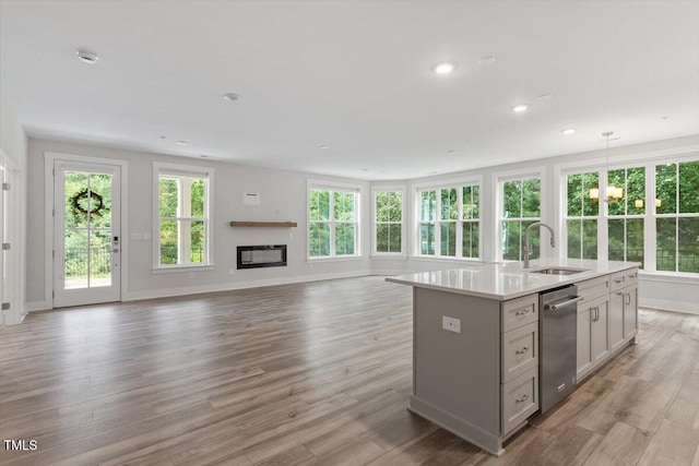 11548 Helmond Way # 104, Raleigh, NC 27617 - kitchen featuring stainless steel dishwasher, light countertops, open floor plan, a glass covered fireplace, and a kitchen island with sink