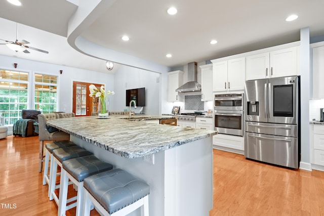 534 Siltstone Pl, Cary, NC 27519 - kitchen with appliances with stainless steel finishes, wall chimney range hood, ceiling fan, light wood-style floors, and decorative backsplash
