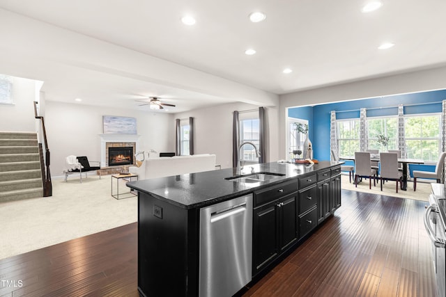 3504 Regent Pines Dr, New Hill, NC 27562 - kitchen with dark cabinets, dishwasher, a kitchen island with sink, a fireplace, and a ceiling fan