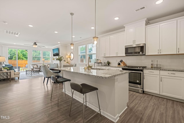 1109 Briar Gate Dr, Holly Springs, NC 27540 - kitchen featuring appliances with stainless steel finishes, open floor plan, wood finished floors, a center island, and white cabinets